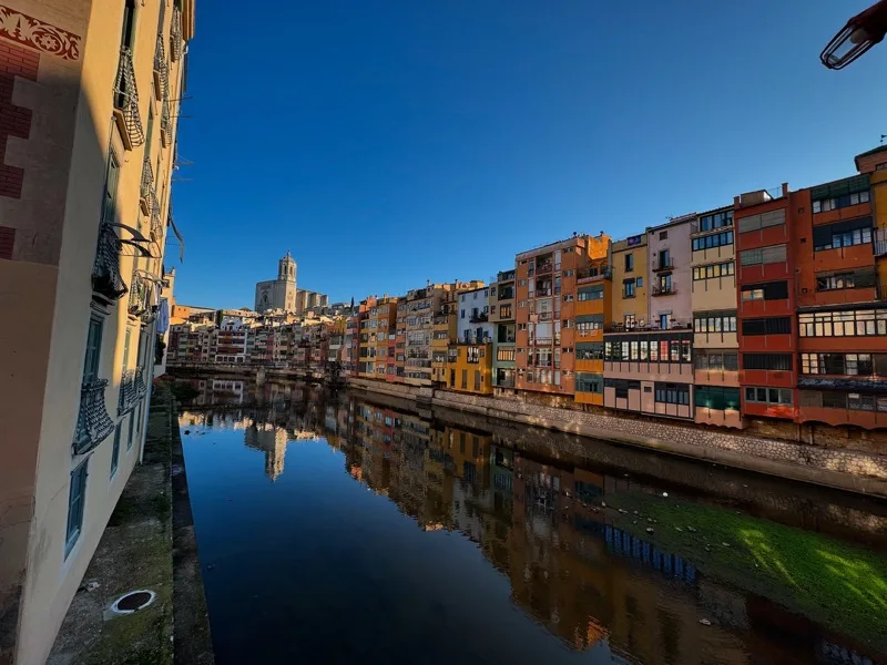 Colourful buildings and a church tower reflected in the river through Girona.