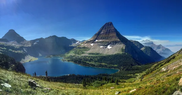 A blue alpine lake beneath a pyramid-shaped peak in Glacier National Park.