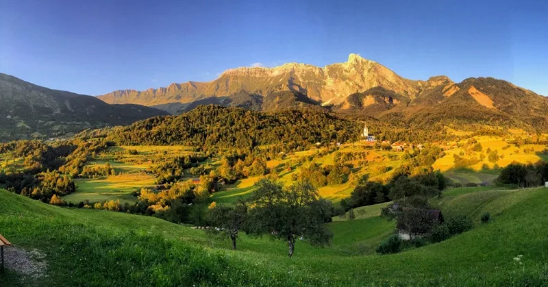 Golden evening light across a mountain ridge, green fields, and a village in Slovenia.